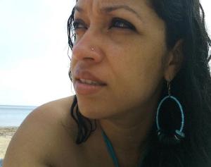 Profile of brown woman with dark hair against sand, sea and sky. 